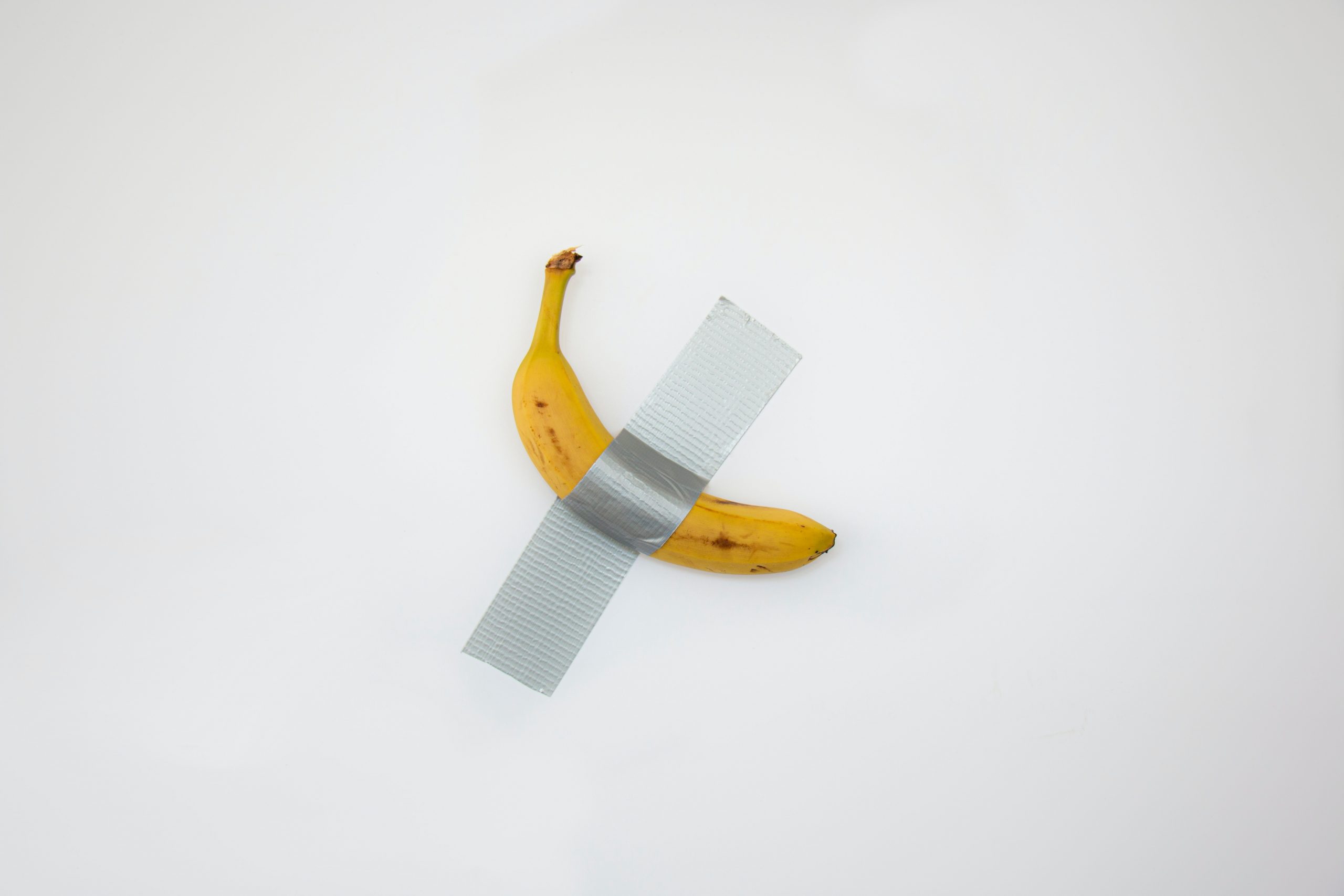 taped yellow banana on white surface